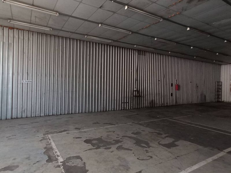 Spacious industrial utility area featuring corrugated metal walls, concrete flooring, and overhead fluorescent lighting, suitable for storage or workshop use.