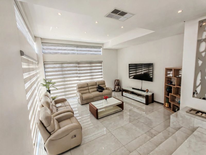Spacious living room featuring high ceilings, large windows with modern roller blinds, recessed downlighting, and polished porcelain floor tiles.