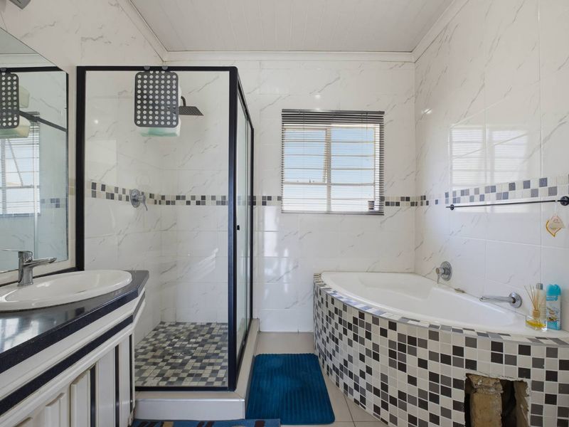 A functional bathroom featuring a glass-enclosed shower, a built-in bathtub with mosaic tiling, and a vanity unit with a countertop basin.
