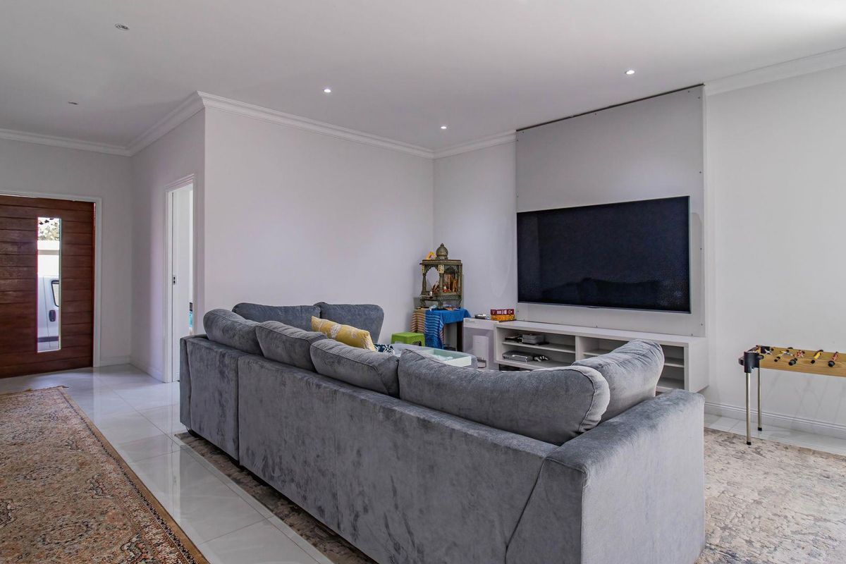 Spacious living room featuring tiled flooring, recessed downlights, and a dedicated media wall, with direct access to the main entrance.