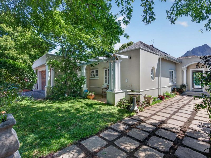 A well-maintained rear exterior view featuring a paved patio area, a pergola with classical columns, and a landscaped garden setting.