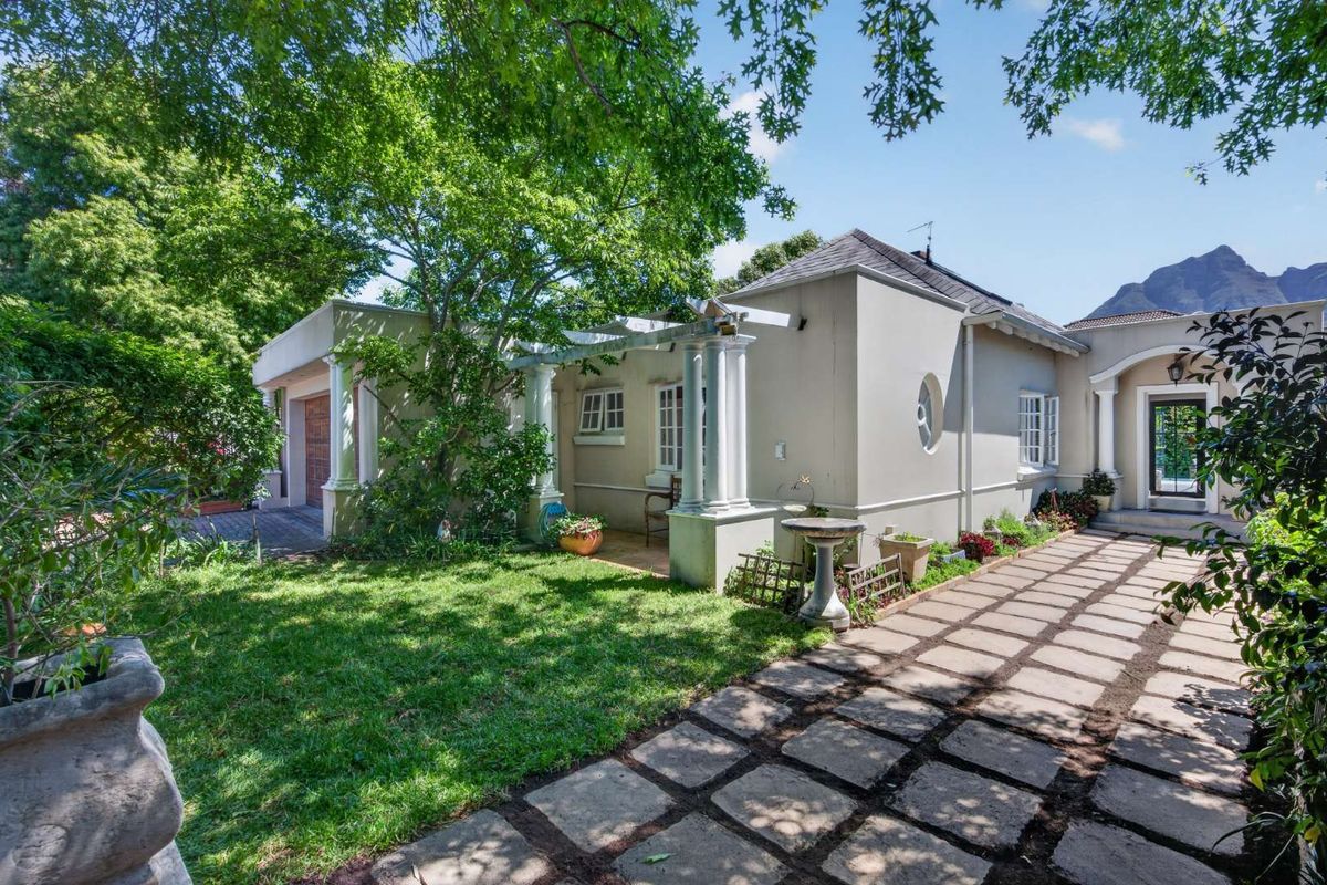 A well-maintained rear exterior view featuring a paved patio area, a pergola with classical columns, and a landscaped garden setting.