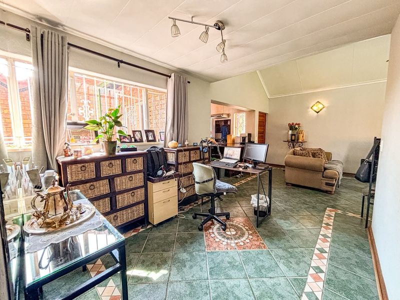 Spacious living area featuring vaulted ceilings, tiled flooring with decorative inlays, and large windows fitted with security bars.