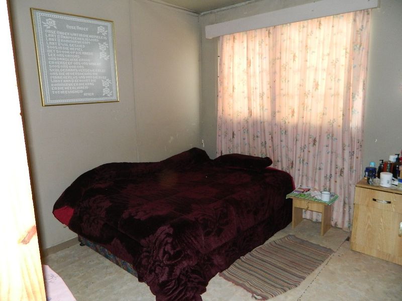 A bedroom featuring neutral wall tones and a window with curtain treatments, requiring cosmetic updates to improve the overall aesthetic and condition.