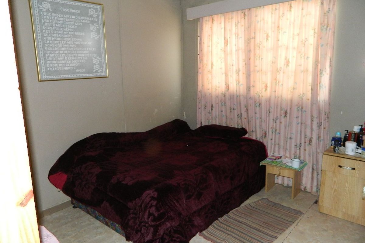 A bedroom featuring neutral wall tones and a window with curtain treatments, requiring cosmetic updates to improve the overall aesthetic and condition.