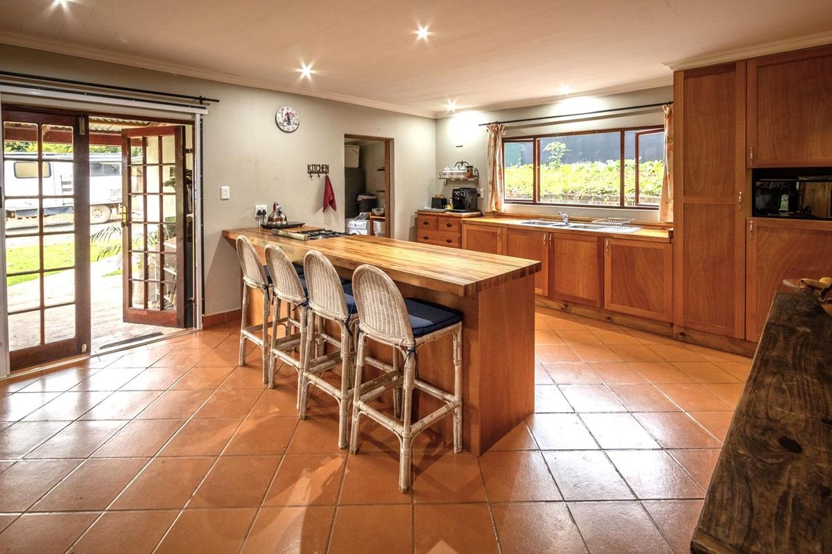 Spacious kitchen featuring wooden cabinetry, a large breakfast bar with integrated hob, tiled flooring, and direct access to the outdoor area.