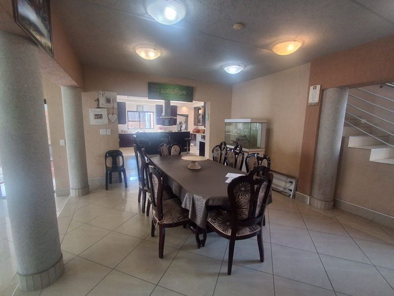 Spacious open-plan dining area featuring tiled floors, structural columns, and a staircase, with a view through to the kitchen area.