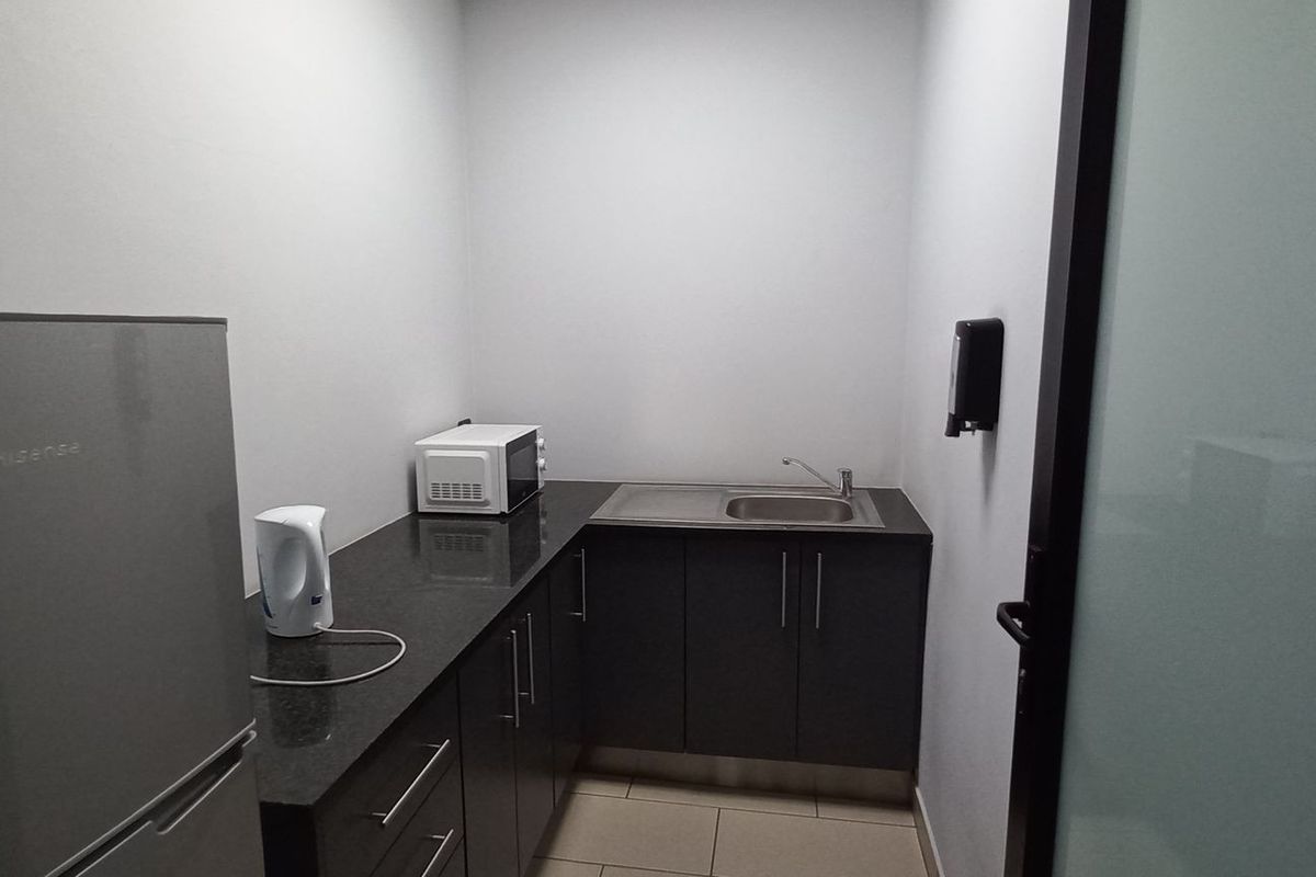 A compact office kitchenette featuring dark cabinetry, granite countertops, a stainless steel sink, and tiled flooring.