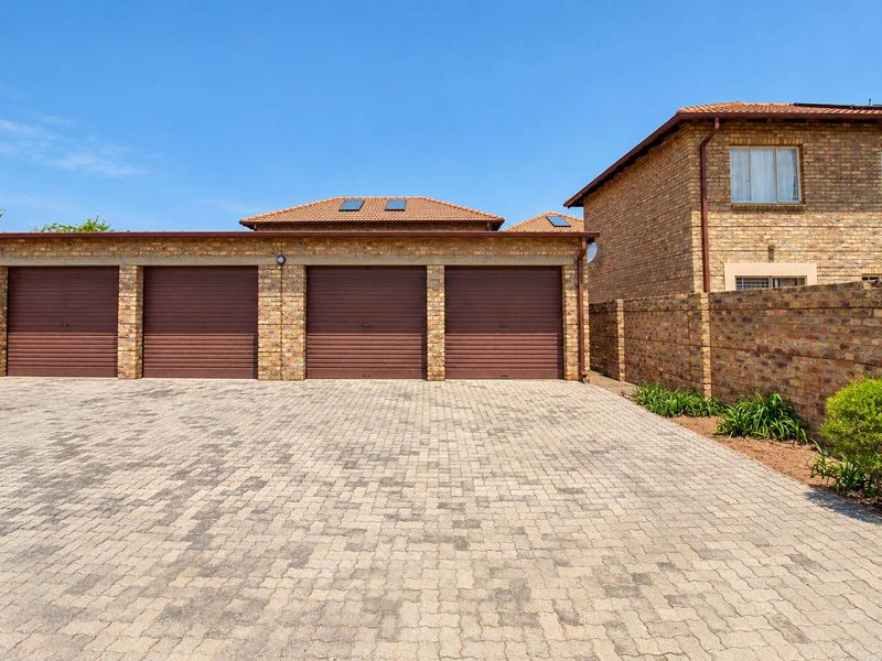 A well-maintained triple garage with roll-up doors, featuring facebrick construction and a spacious paved driveway in a secure townhouse setting.