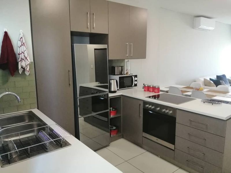 Modern open-plan kitchen featuring sleek cabinetry, integrated appliances, and tiled flooring, seamlessly flowing into the adjacent living and dining area.