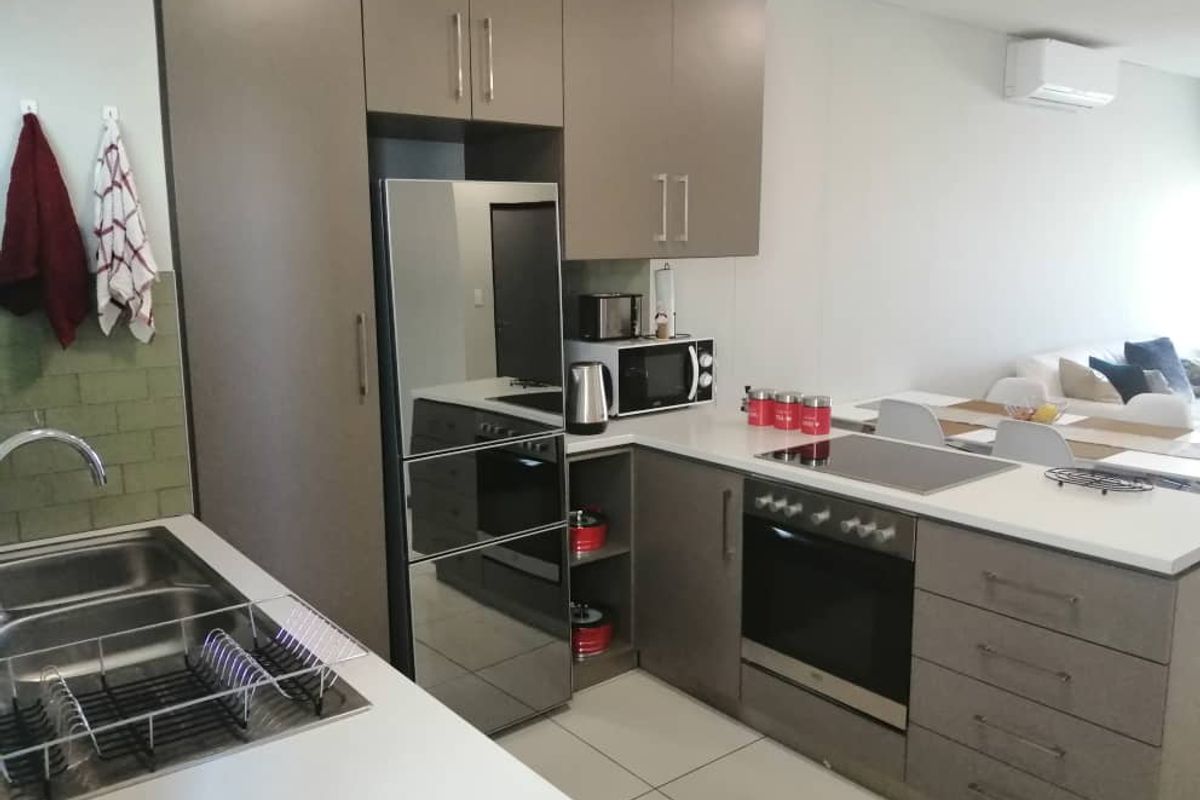 Modern open-plan kitchen featuring sleek cabinetry, integrated appliances, and tiled flooring, seamlessly flowing into the adjacent living and dining area.