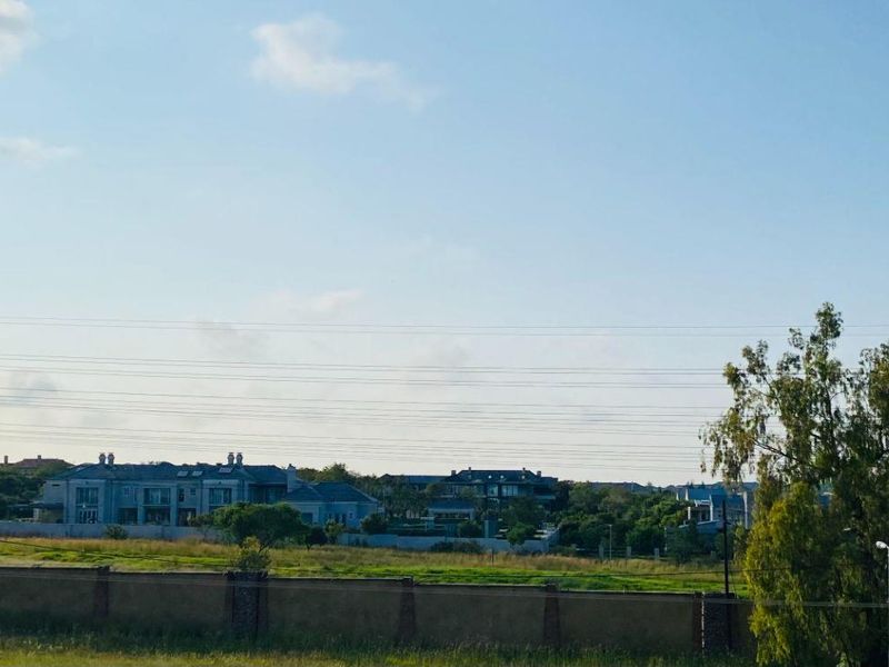 A wide-angle view of the surrounding neighbourhood and landscape, featuring a perimeter wall and distant residential properties.