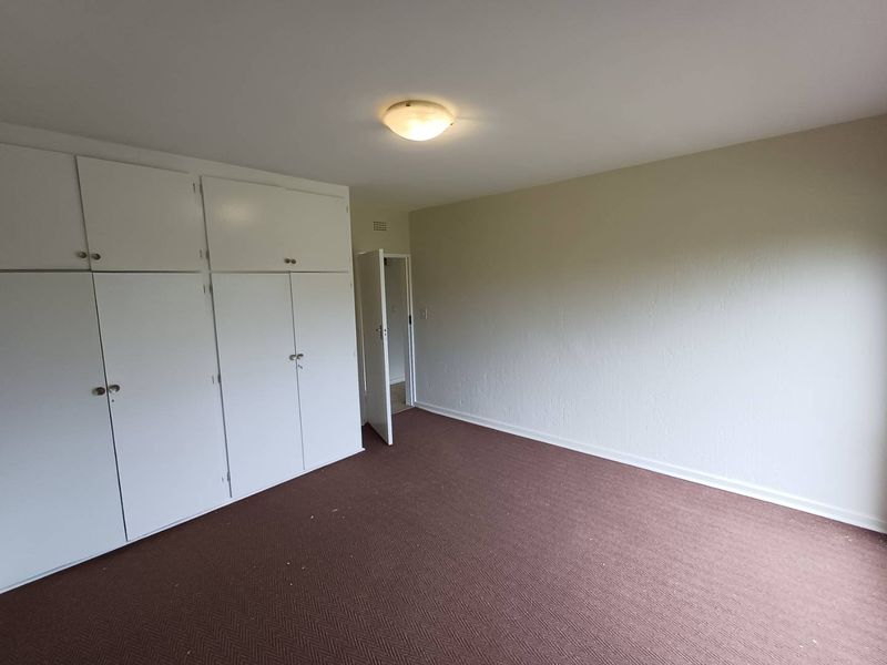 A spacious, empty bedroom featuring neutral walls, carpet flooring, and extensive built-in cupboard storage.