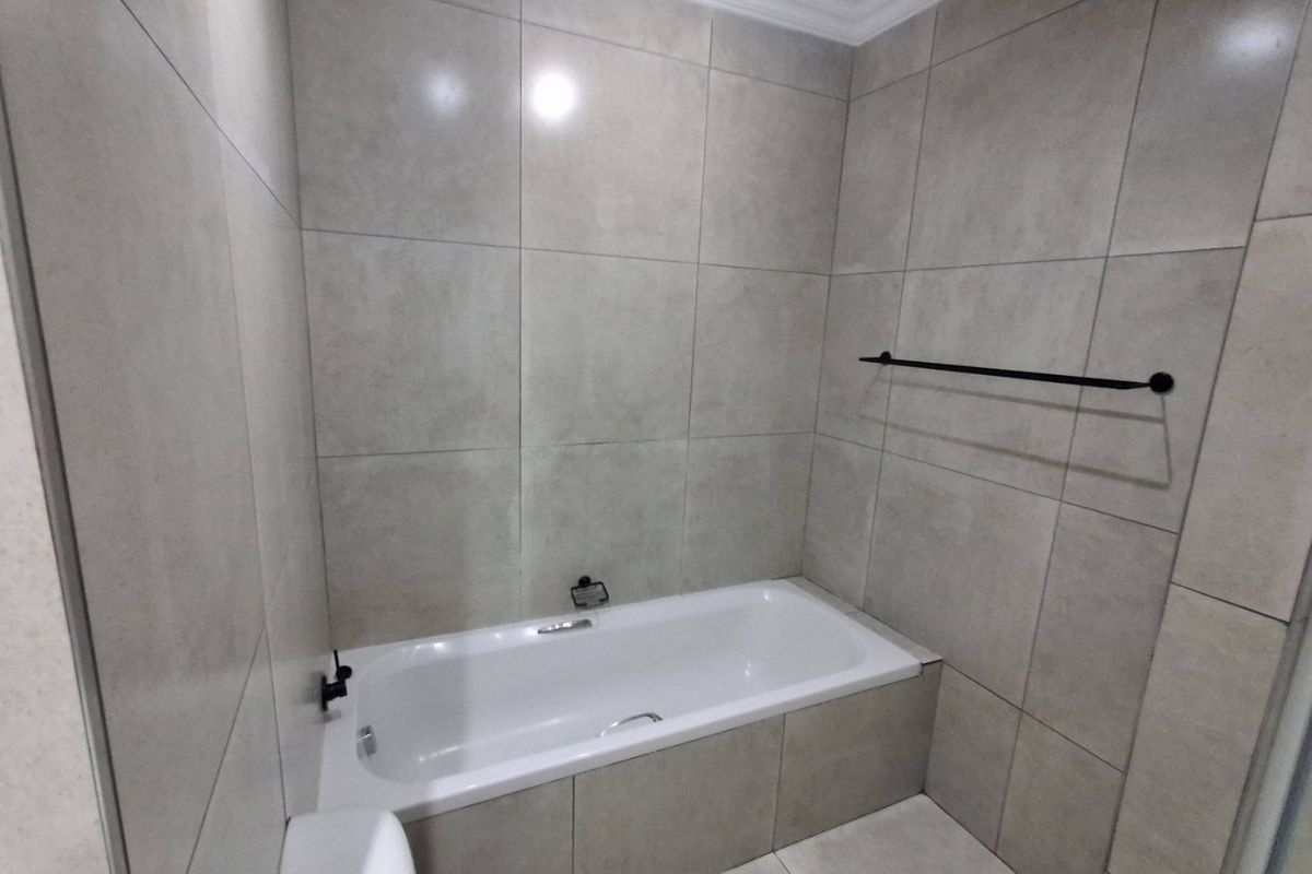 A modern, neutral-toned bathroom featuring large-format wall and floor tiles, a built-in bathtub, and a sleek black towel rail.