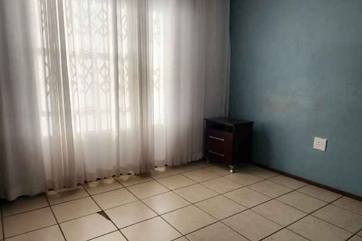A bedroom featuring tiled flooring, a blue accent wall, and security bars on the window.