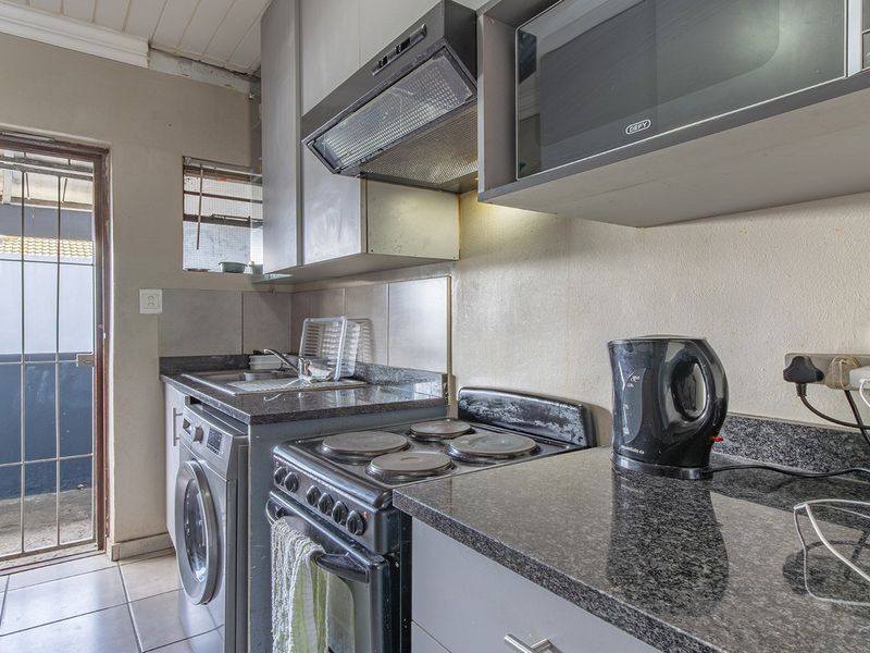 Compact kitchen featuring granite countertops, built-in cabinetry, an electric stove, extractor fan, and integrated microwave, with direct access to an exterior area.