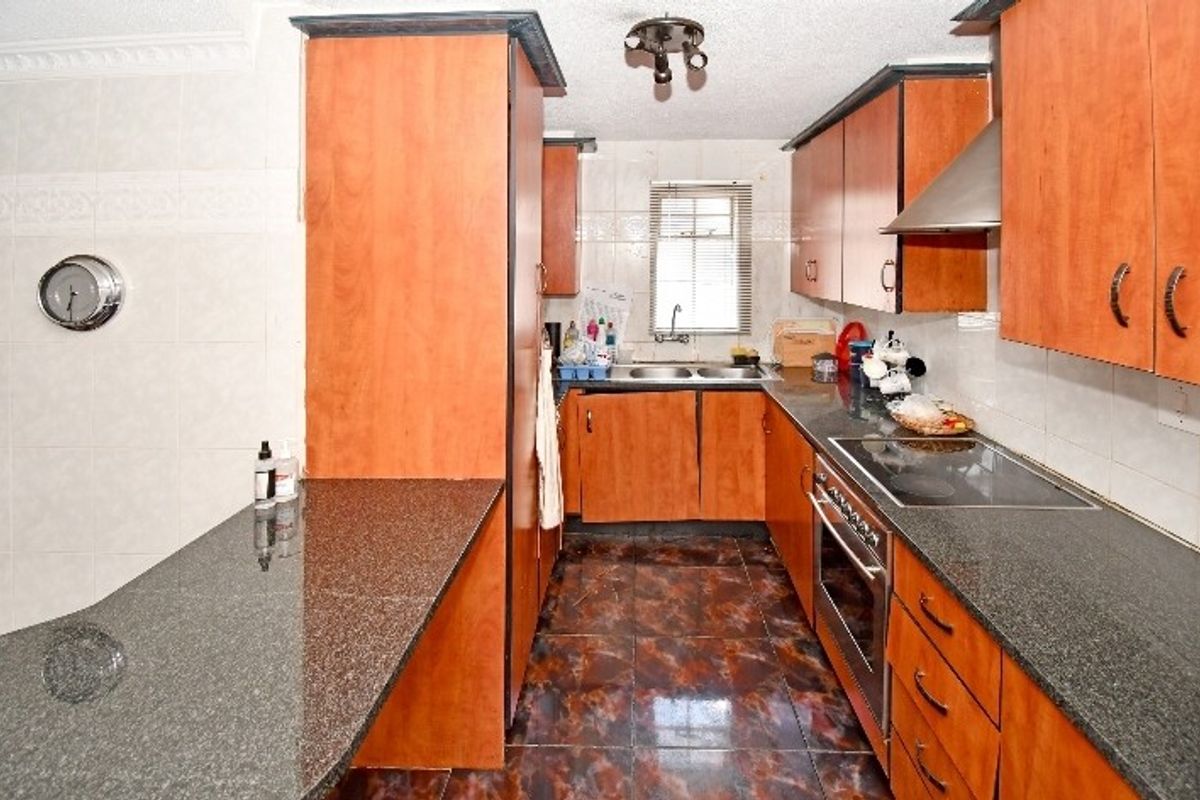 A functional kitchen featuring wood-finish cabinetry, granite countertops, integrated oven and hob, and tiled flooring with a practical layout.