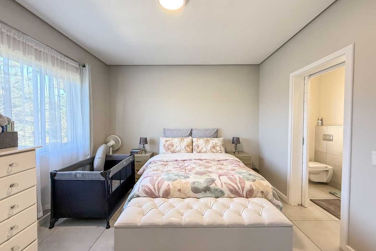 A well-maintained bedroom featuring neutral wall tones, tiled flooring, and an en-suite bathroom accessible through a sliding door.
