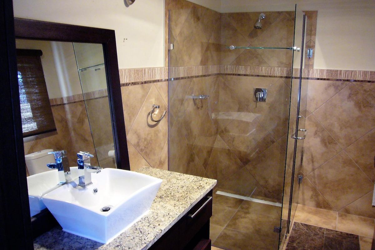 Modern bathroom featuring a granite vanity top with a vessel sink, a glass-enclosed walk-in shower, and neutral-toned wall and floor tiling.