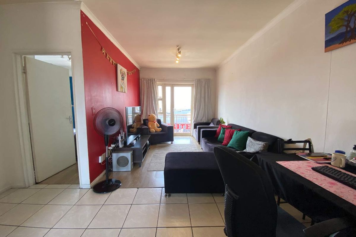 A living room featuring tiled flooring, a prominent red accent wall, and access to a balcony through a glass door.