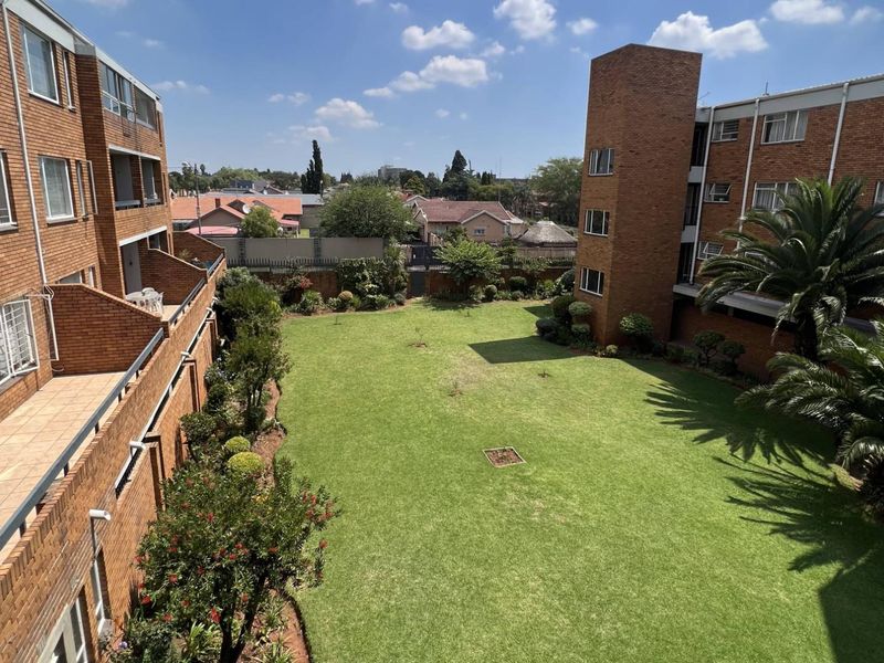 Elevated view of the apartment complex rear courtyard featuring a well-maintained central lawn, landscaped garden beds, and brick building facades with balconies.