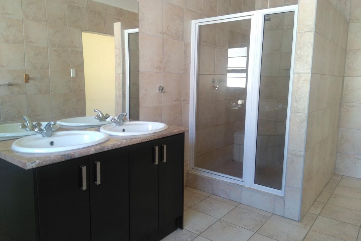 A functional bathroom featuring a double vanity with dark cabinetry, a large wall mirror, and a separate walk-in shower with tiled enclosure.