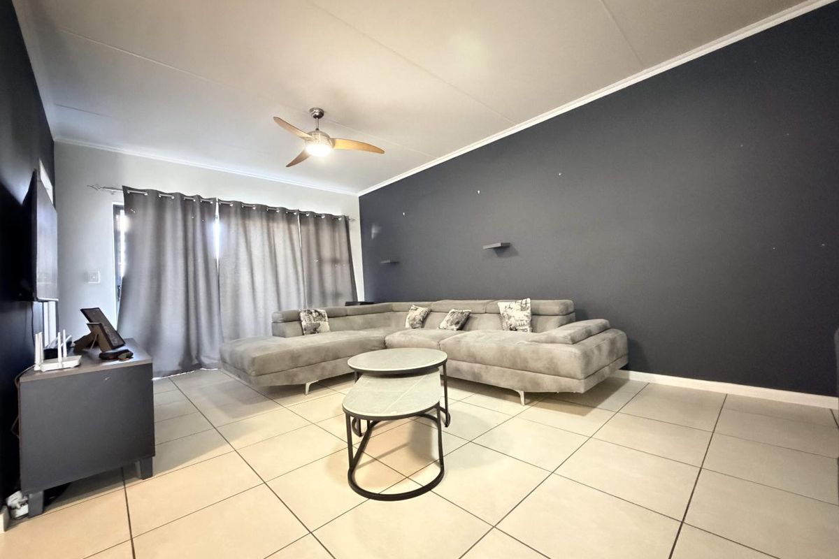 A spacious living room featuring large floor tiles, a ceiling fan, and a dark accent wall with sliding door access to the exterior.
