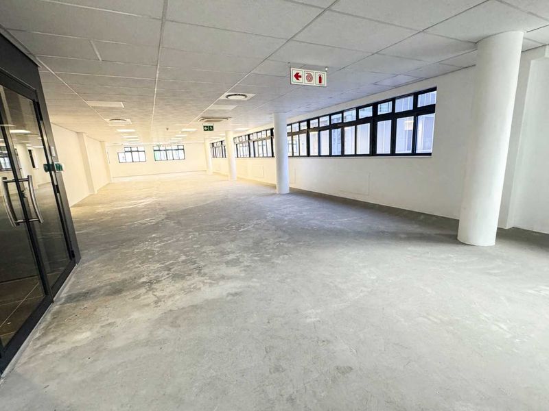 A spacious, open-plan office area featuring a suspended ceiling, large windows providing natural light, and structural columns, ready for custom fit-out.