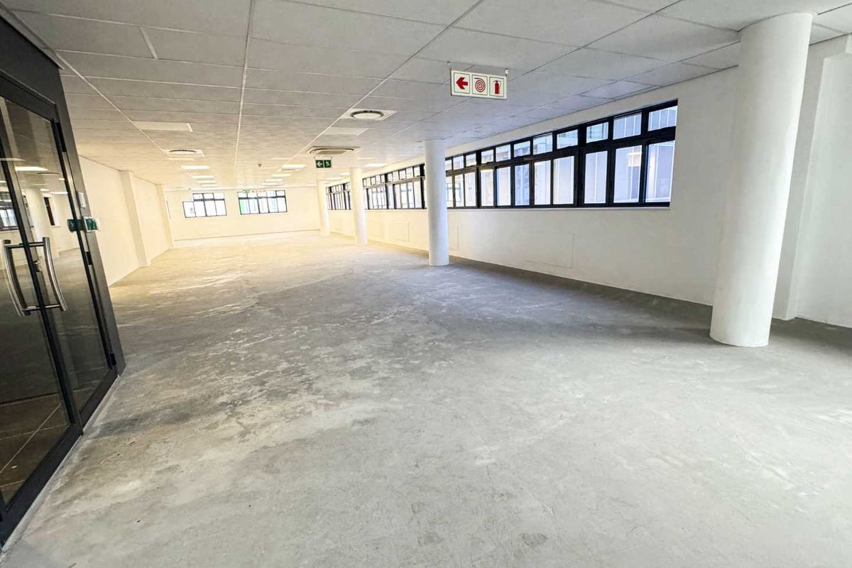 A spacious, open-plan office area featuring a suspended ceiling, large windows providing natural light, and structural columns, ready for custom fit-out.