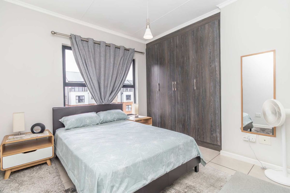 A well-maintained bedroom featuring built-in dark wood-grain wardrobes, tiled flooring, and a large window providing natural light.