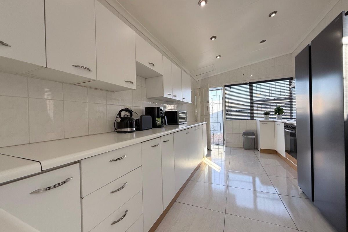 A clean, functional kitchen featuring white cabinetry, tiled flooring, a tiled backsplash, and recessed lighting, with direct access to an exterior security gate.