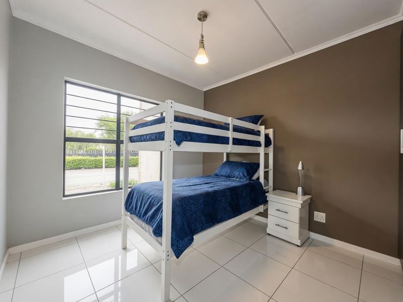 A well-maintained bedroom featuring tiled flooring, a large window with security bars, and neutral wall tones.