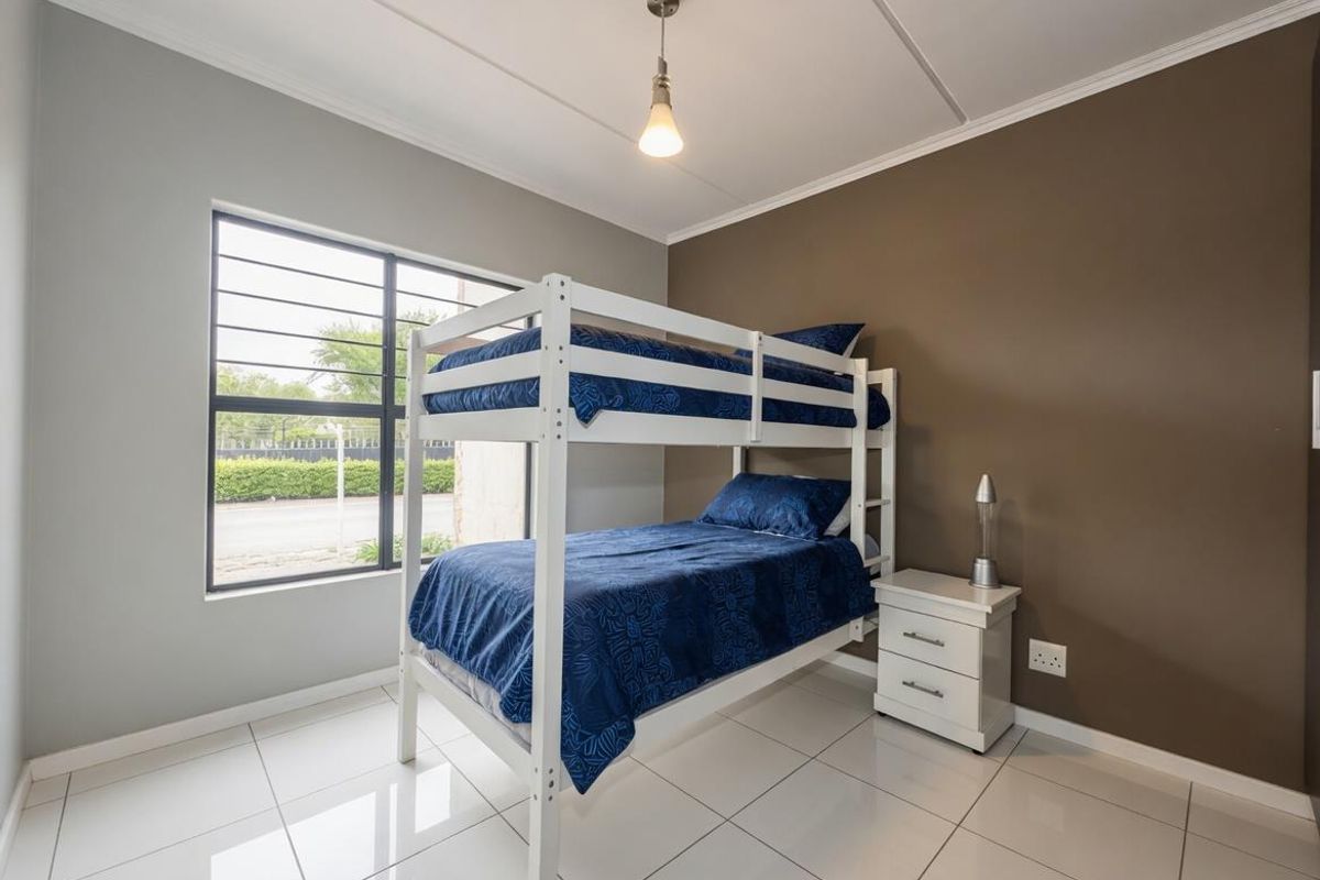 A well-maintained bedroom featuring tiled flooring, a large window with security bars, and neutral wall tones.