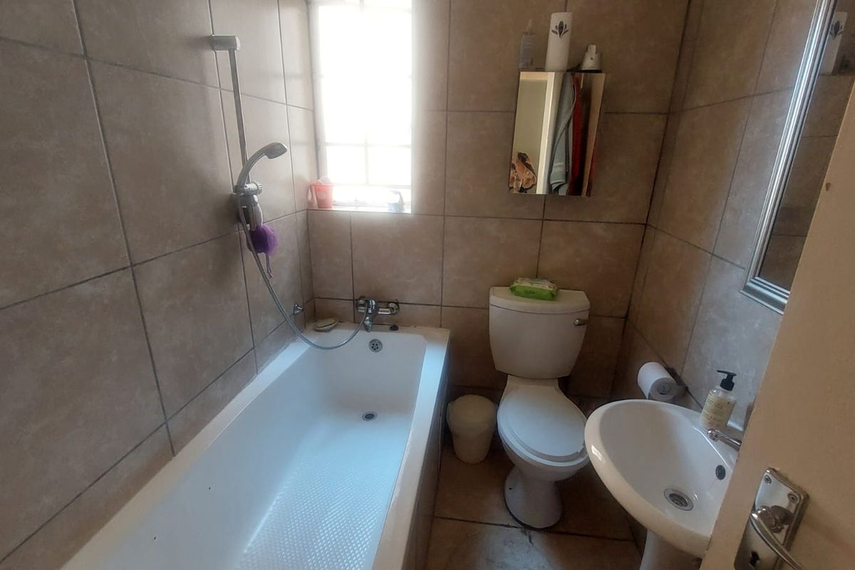 A functional bathroom featuring a bathtub with shower attachment, pedestal basin, and toilet, finished with neutral wall and floor tiling.