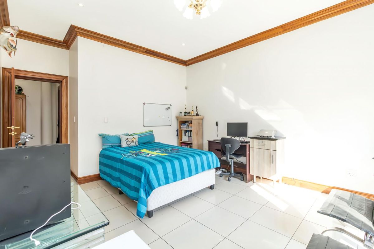 A spacious bedroom featuring tiled flooring, wooden crown molding, and recessed lighting, providing a functional living space.