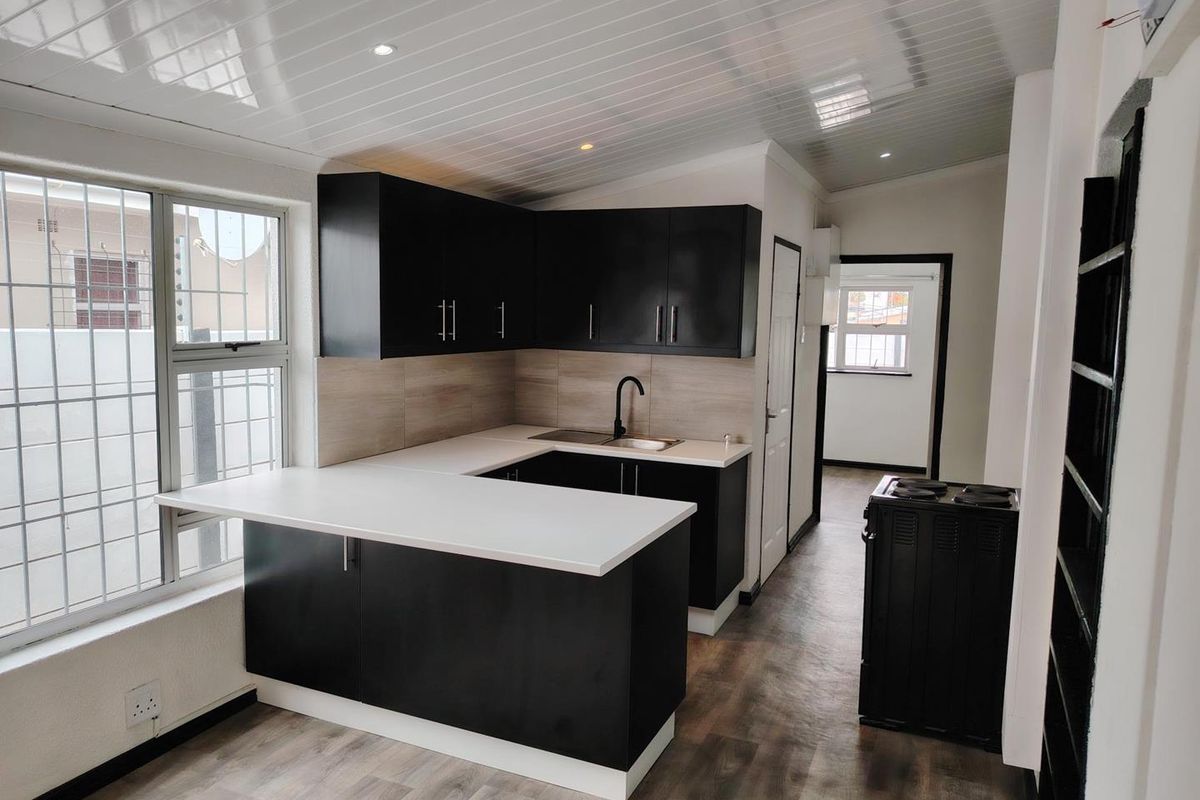 Modern kitchen featuring black cabinetry, white countertops, stainless steel sink, and vinyl flooring, offering a clean and functional workspace.