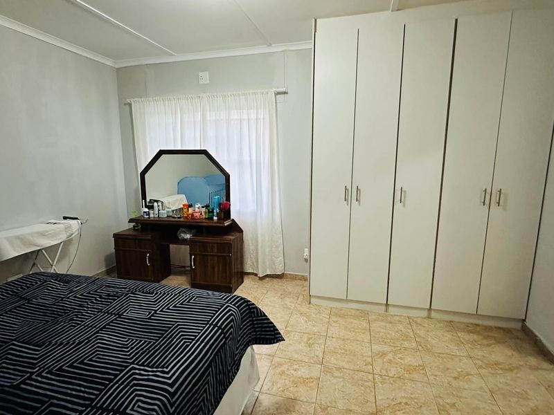 A bedroom featuring built-in cupboards, tiled flooring, and a coved ceiling, with an adjacent en-suite bathroom entrance.