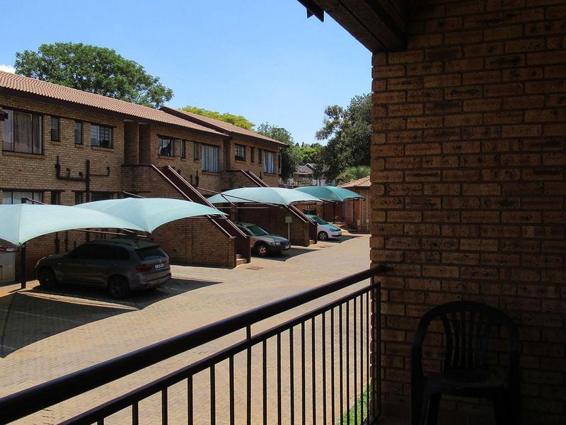 View from a balcony overlooking the apartment complex parking area with brick facade buildings and shade cloth carports.