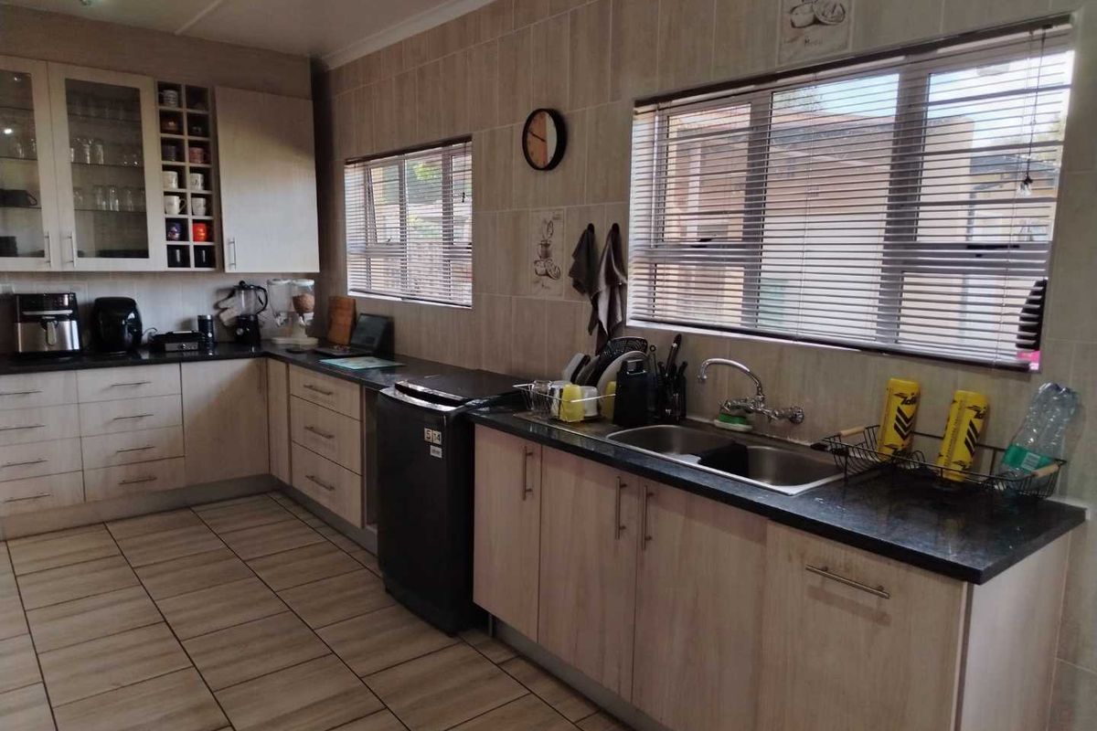 A functional kitchen featuring light wood-finish cabinetry, dark granite countertops, tiled flooring, and a double-basin stainless steel sink with large windows.