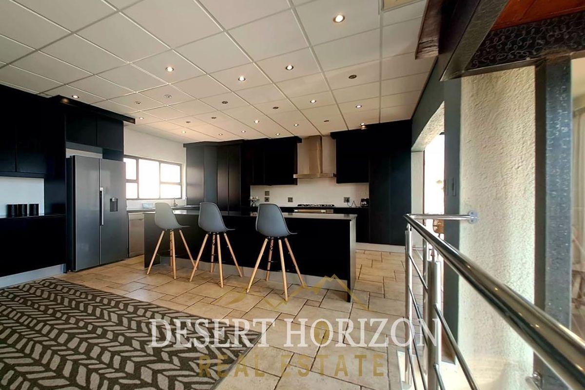 Modern kitchen featuring dark cabinetry, a central island, stainless steel extractor fan, and recessed lighting, finished with tiled flooring.
