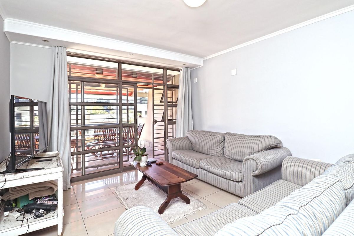 A bright living room featuring large sliding glass doors that open onto a private balcony, with neutral tiled flooring throughout.