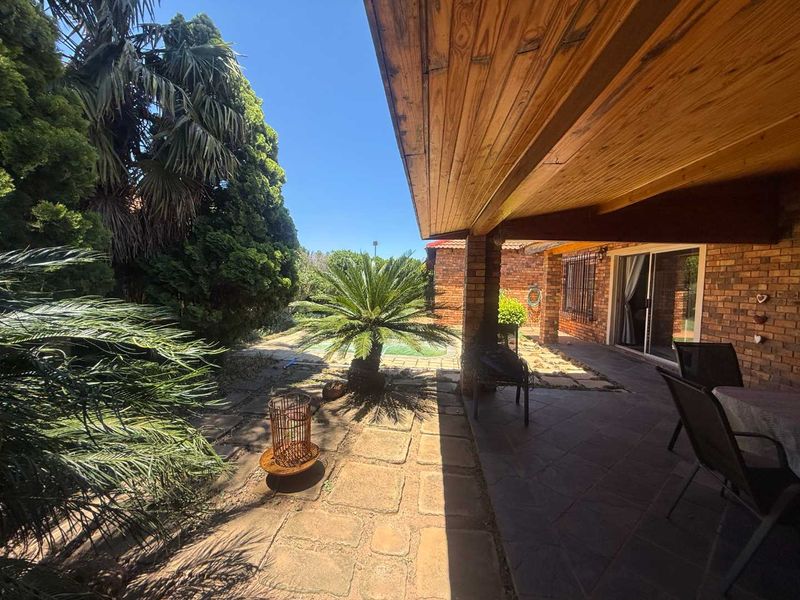 A covered patio area featuring a timber ceiling, brick pillars, and tiled flooring, providing direct access to the garden and pool area.