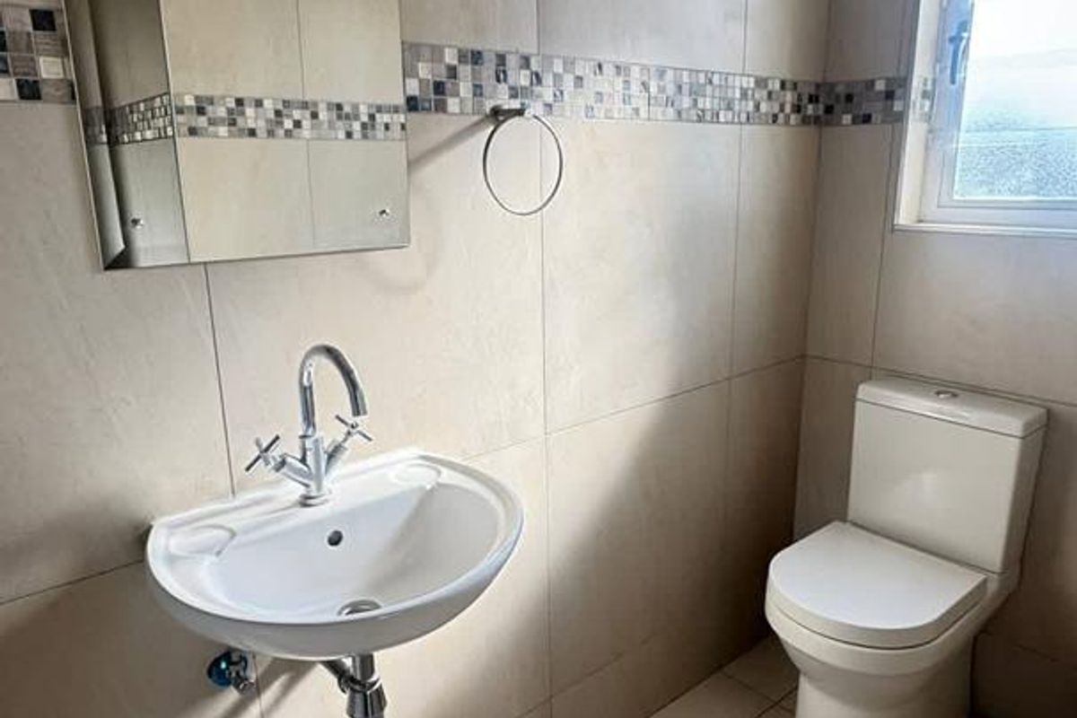 A clean, modern bathroom featuring floor-to-ceiling neutral tiling, a wall-mounted basin with chrome fixtures, and a standard toilet.