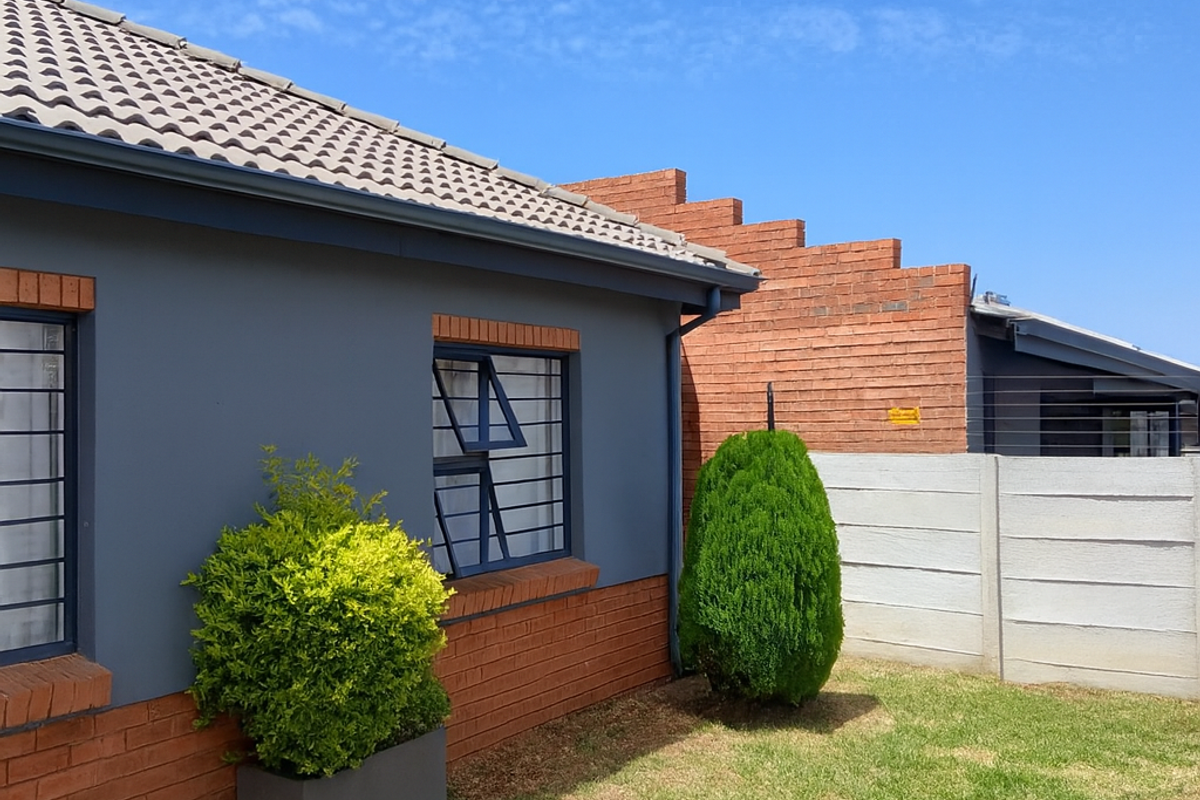 A view of the rear exterior of the house, featuring a grey painted facade with brick accents, security bars on windows, and a lawn area.
