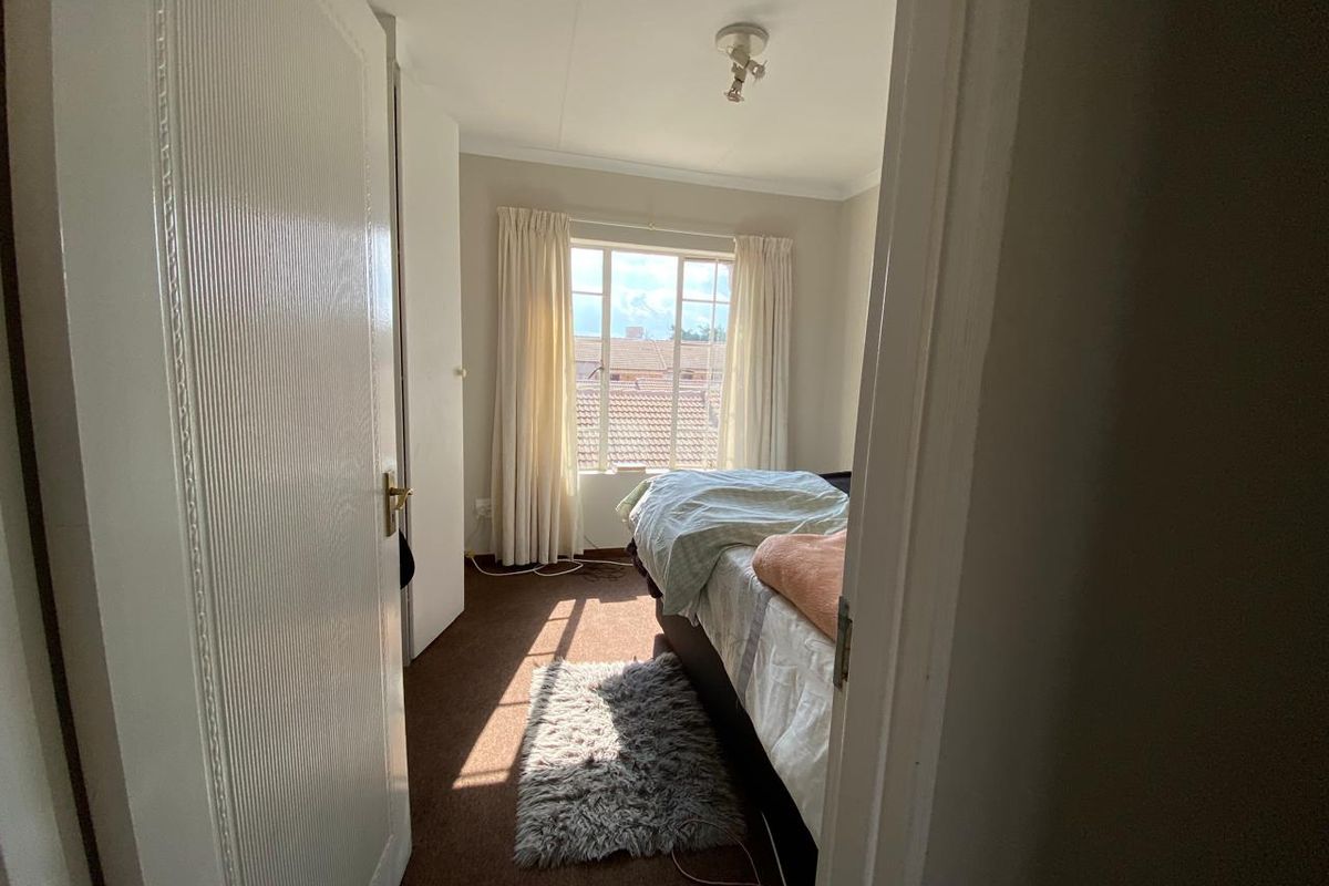 A bedroom featuring brown carpeting, built-in wardrobe storage, and a window providing natural light and a view of the surrounding neighborhood.