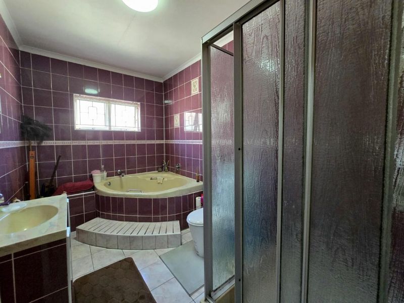 A dated bathroom featuring a corner bathtub, separate shower enclosure, and vanity basin, finished with purple wall tiles and neutral floor tiling.