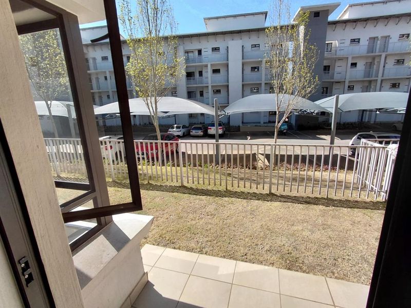 A ground floor patio area featuring tiled flooring and a metal balustrade, overlooking a parking area with shade cloth carports.