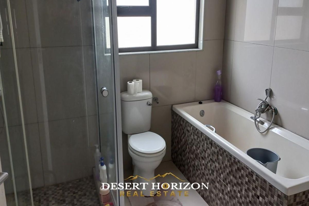 A functional bathroom featuring a glass-enclosed shower, a built-in bathtub with mosaic tile detailing, and a standard toilet.