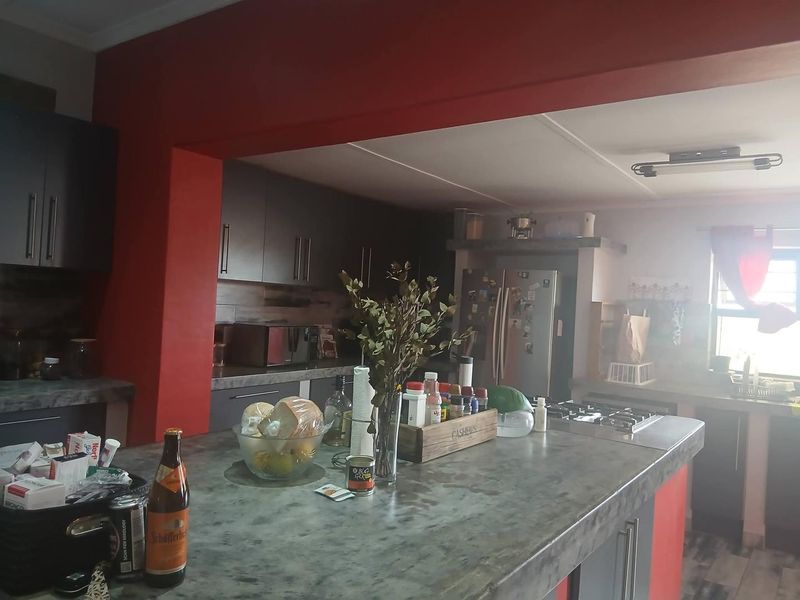 A functional kitchen featuring a large central island with stone countertops, dark cabinetry, and a built-in gas hob with an overhead extractor fan.