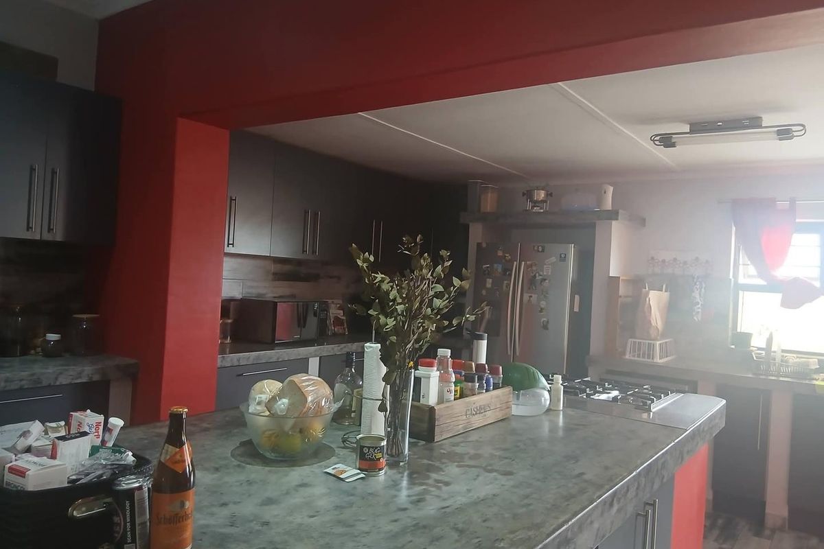 A functional kitchen featuring a large central island with stone countertops, dark cabinetry, and a built-in gas hob with an overhead extractor fan.